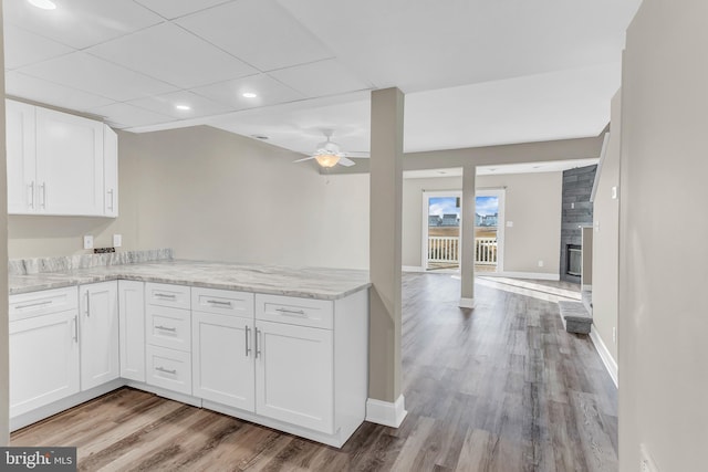 kitchen with ceiling fan, light stone countertops, a fireplace, white cabinets, and light wood-type flooring