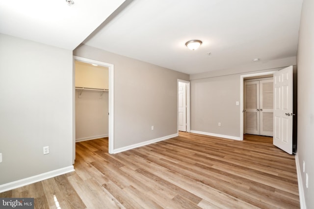 unfurnished bedroom featuring light wood-type flooring, a spacious closet, and a closet