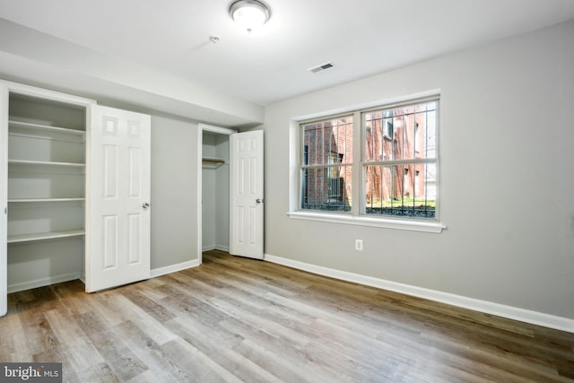 unfurnished bedroom with light hardwood / wood-style floors and two closets