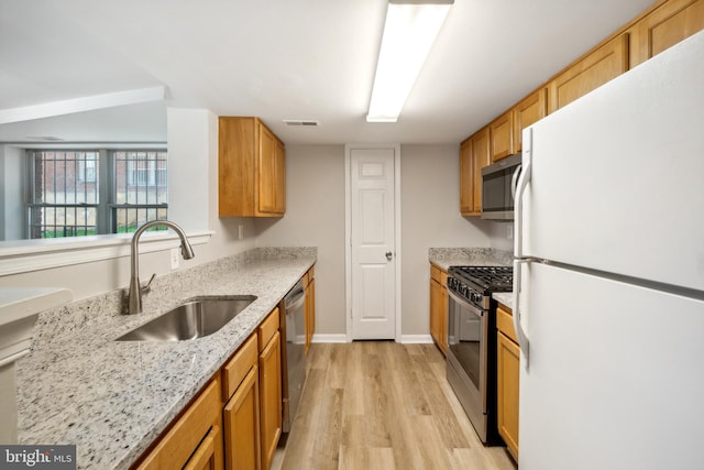 kitchen featuring stainless steel appliances, light stone counters, light hardwood / wood-style floors, and sink