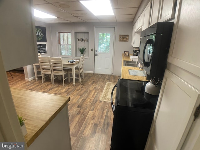 kitchen featuring hardwood / wood-style floors, a drop ceiling, black appliances, sink, and white cabinetry