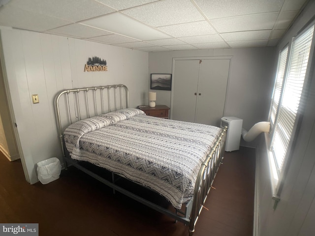 bedroom with a paneled ceiling, wooden walls, a closet, and dark wood-type flooring