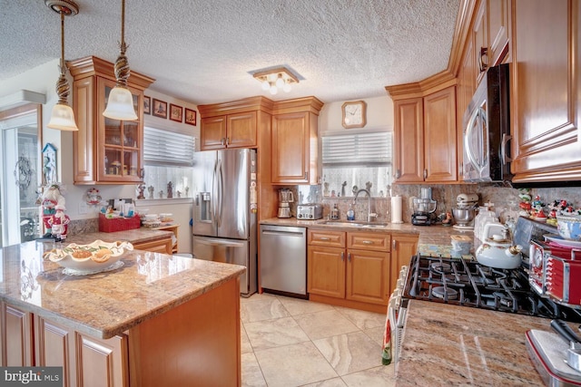 kitchen with light stone countertops, backsplash, stainless steel appliances, sink, and decorative light fixtures