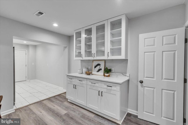 bar featuring white cabinets, light stone counters, and light hardwood / wood-style flooring