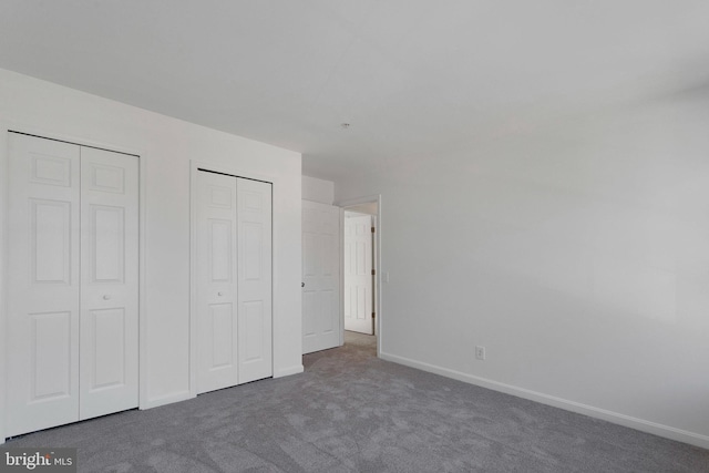 unfurnished bedroom with two closets and dark carpet