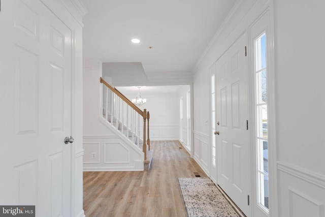 foyer with crown molding, light hardwood / wood-style floors, and a chandelier