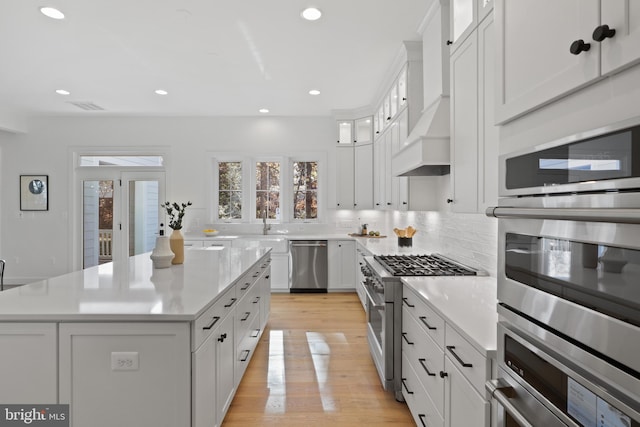 kitchen with a center island, stainless steel appliances, white cabinetry, and light hardwood / wood-style flooring