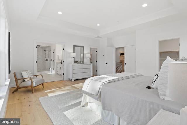 bedroom with ensuite bath, a spacious closet, light wood-type flooring, a tray ceiling, and a closet