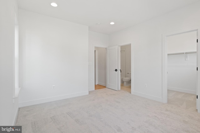 unfurnished bedroom with a walk in closet, ensuite bathroom, a closet, and light colored carpet