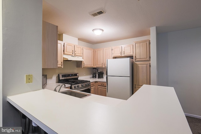 kitchen with sink, stainless steel gas stove, light brown cabinets, white refrigerator, and kitchen peninsula