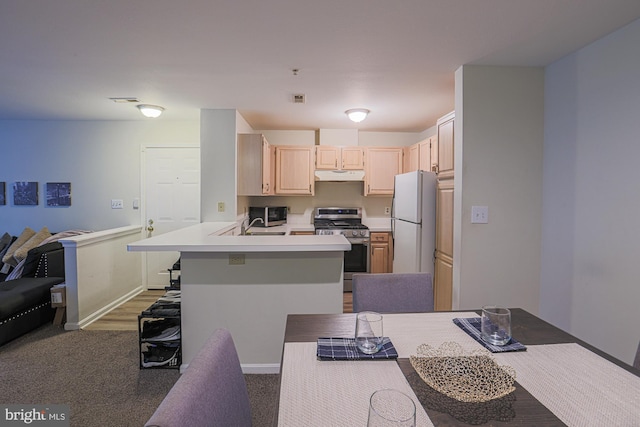 kitchen featuring a breakfast bar, refrigerator, stainless steel gas range oven, kitchen peninsula, and light brown cabinets