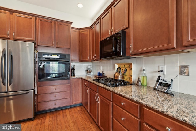 kitchen featuring light hardwood / wood-style floors, decorative backsplash, light stone counters, and black appliances