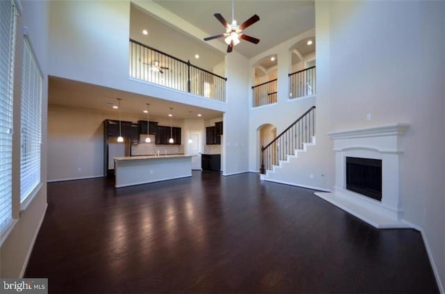 unfurnished living room featuring ceiling fan, dark hardwood / wood-style flooring, and a high ceiling