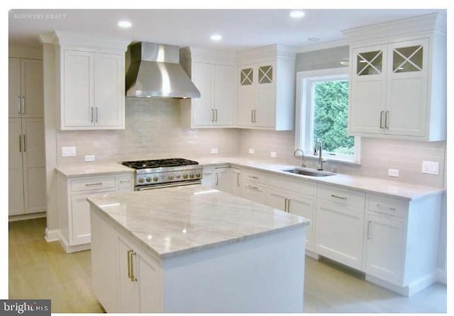 kitchen featuring sink, high end stainless steel range oven, wall chimney range hood, light stone counters, and white cabinets