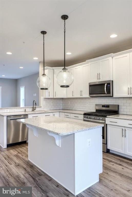 kitchen with appliances with stainless steel finishes, white cabinetry, hanging light fixtures, and a kitchen island