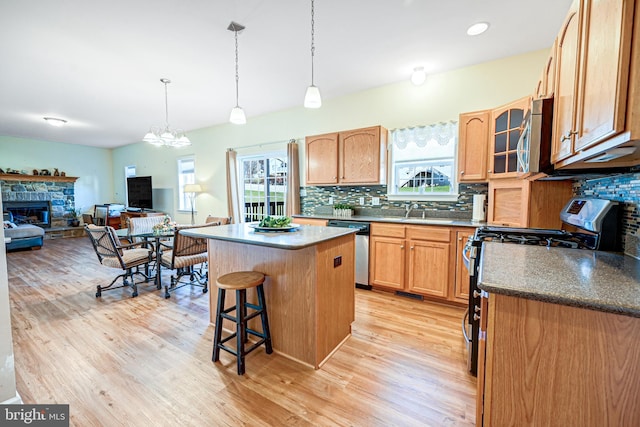 kitchen with stainless steel appliances, tasteful backsplash, a stone fireplace, light hardwood / wood-style floors, and a kitchen island