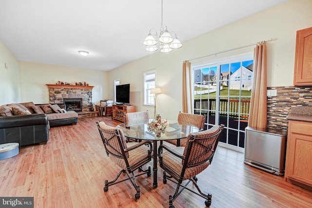 dining space with a stone fireplace, light hardwood / wood-style floors, and a notable chandelier