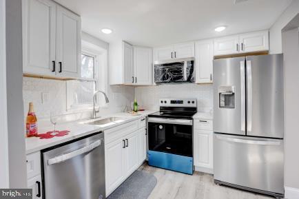 kitchen featuring stainless steel appliances, white cabinetry, light hardwood / wood-style floors, and sink