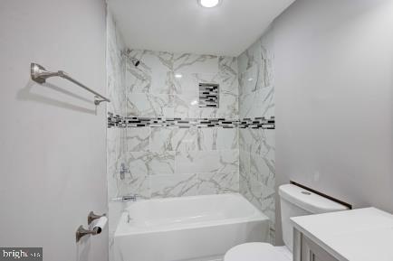 full bathroom featuring vanity, tiled shower / bath combo, and toilet