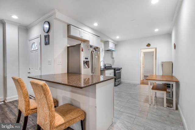 kitchen with a kitchen bar, ornamental molding, stainless steel appliances, wall chimney range hood, and white cabinetry