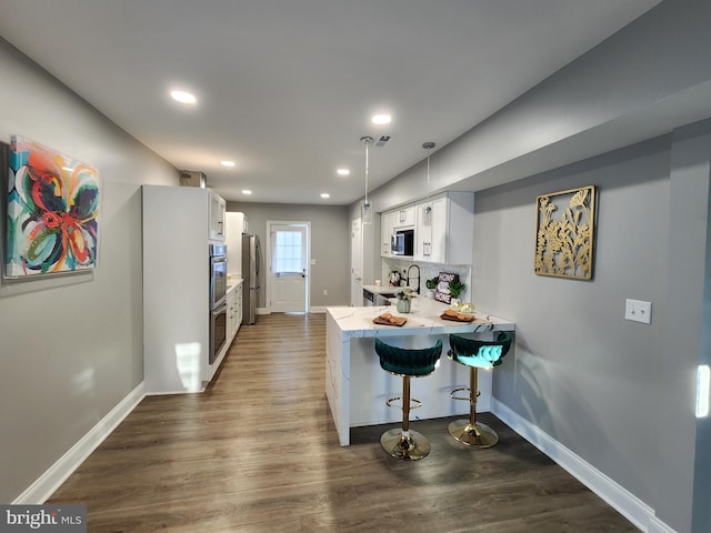 kitchen featuring kitchen peninsula, appliances with stainless steel finishes, a kitchen breakfast bar, white cabinets, and dark hardwood / wood-style floors