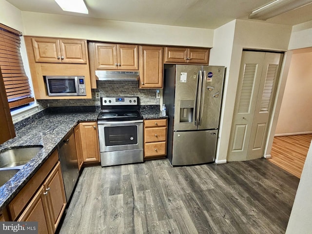 kitchen featuring appliances with stainless steel finishes, backsplash, sink, dark stone countertops, and hardwood / wood-style floors