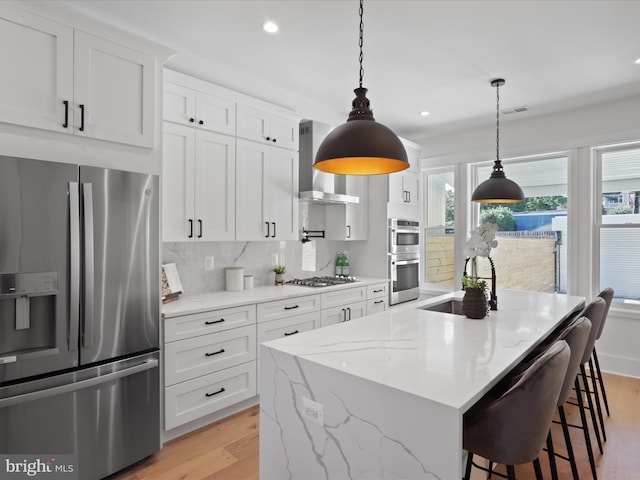 kitchen with white cabinets, stainless steel appliances, wall chimney range hood, and light wood-type flooring