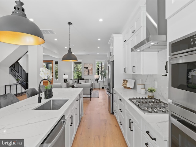 kitchen featuring white cabinets, appliances with stainless steel finishes, wall chimney exhaust hood, and sink