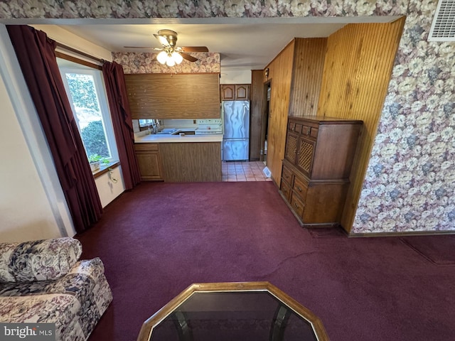 kitchen featuring carpet flooring, stainless steel fridge, ceiling fan, wooden walls, and sink