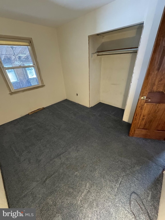 unfurnished bedroom with dark carpet and a closet