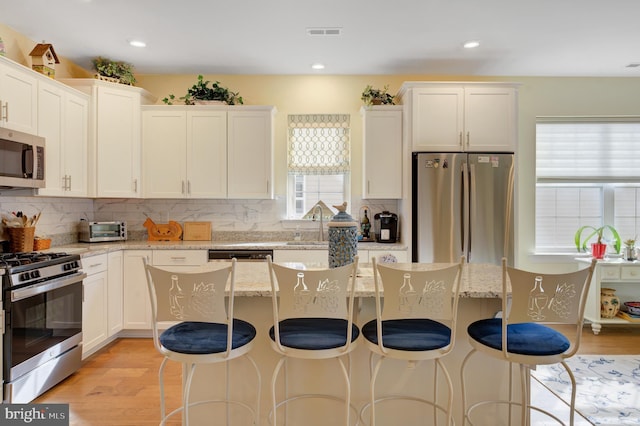 kitchen featuring light stone countertops, appliances with stainless steel finishes, light hardwood / wood-style flooring, white cabinets, and a kitchen island