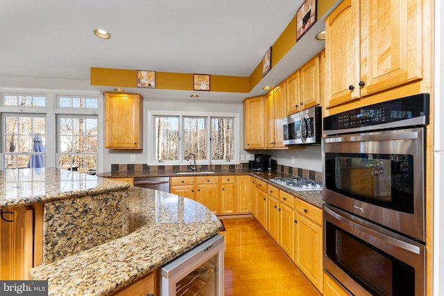 kitchen with light stone countertops, sink, beverage cooler, stainless steel appliances, and light wood-type flooring