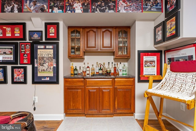 bar with sink, dark stone counters, and light hardwood / wood-style flooring