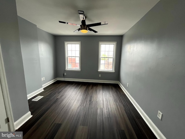 spare room featuring baseboards, visible vents, ceiling fan, and dark wood-style flooring