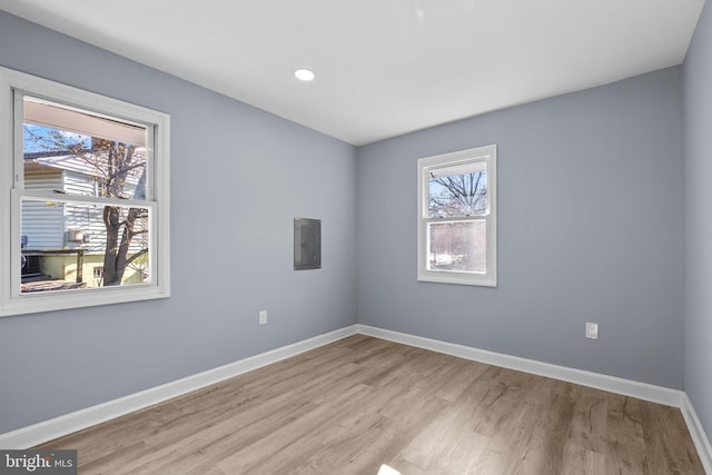 empty room with electric panel, a healthy amount of sunlight, and light hardwood / wood-style floors