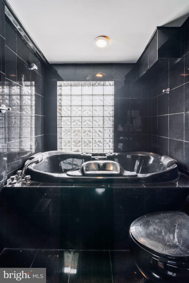 bathroom with tile patterned flooring, tiled bath, toilet, and tile walls