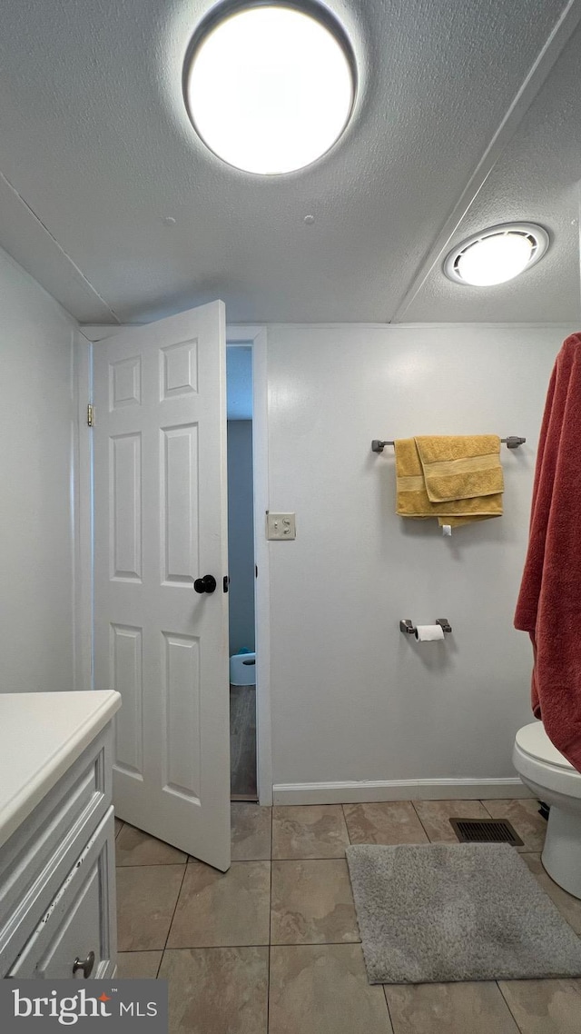 bathroom with a textured ceiling, tile patterned floors, vanity, and toilet