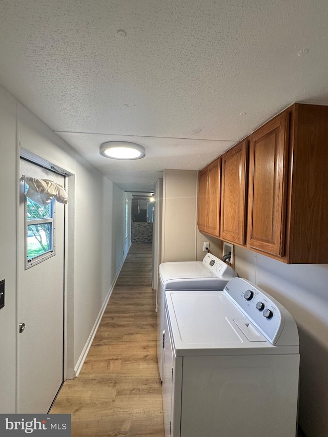laundry room with cabinet space, light wood finished floors, washing machine and clothes dryer, a textured ceiling, and baseboards