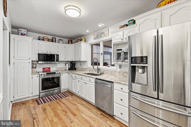 kitchen with light stone countertops, sink, stainless steel appliances, light hardwood / wood-style flooring, and white cabinets