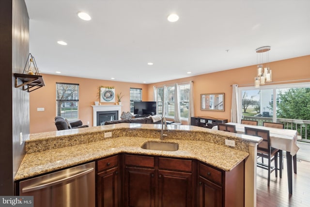 kitchen with light stone counters, sink, decorative light fixtures, light hardwood / wood-style flooring, and dishwasher