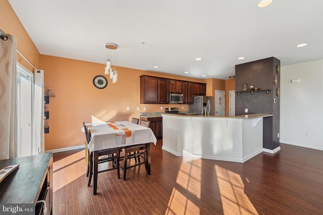 kitchen with light stone countertops, appliances with stainless steel finishes, hanging light fixtures, and dark wood-type flooring