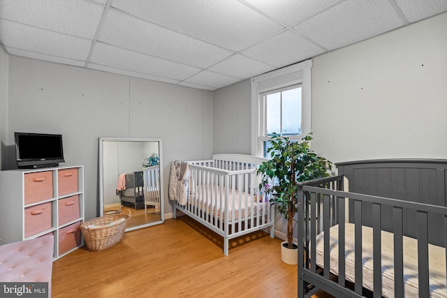 bedroom featuring a paneled ceiling, hardwood / wood-style flooring, and a nursery area