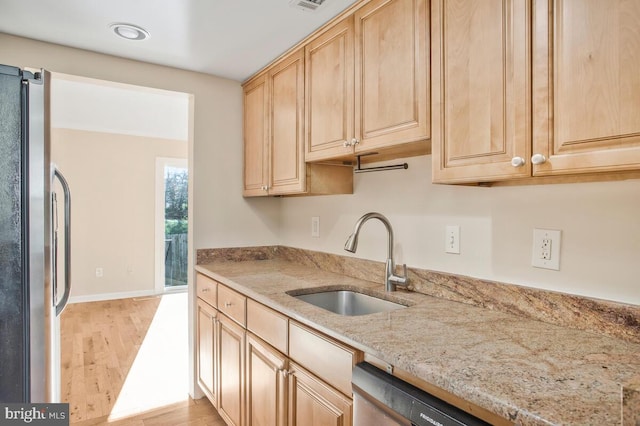 kitchen with light brown cabinets, sink, light stone countertops, appliances with stainless steel finishes, and light hardwood / wood-style floors