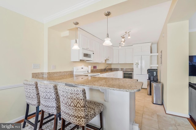 kitchen with a breakfast bar, white appliances, kitchen peninsula, decorative light fixtures, and white cabinetry