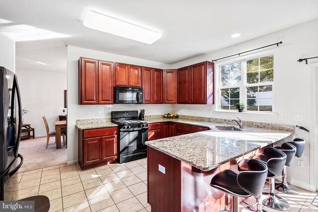 kitchen with black appliances, light stone counters, kitchen peninsula, and sink