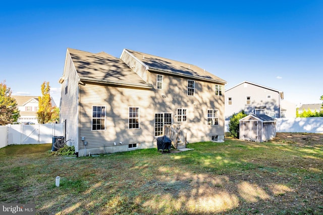 rear view of property with a lawn, central AC unit, and a storage shed