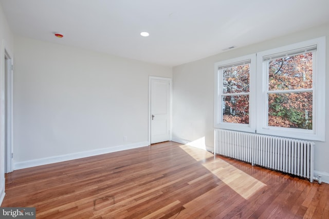 unfurnished room featuring radiator heating unit and hardwood / wood-style flooring