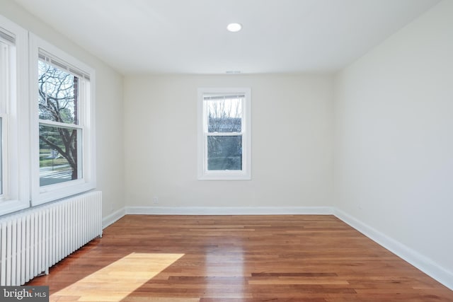 unfurnished room featuring a wealth of natural light, radiator, and wood-type flooring