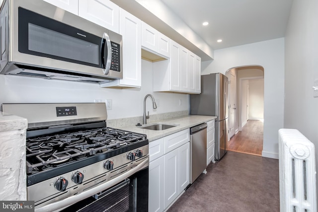 kitchen featuring stainless steel appliances, light stone counters, radiator, and sink