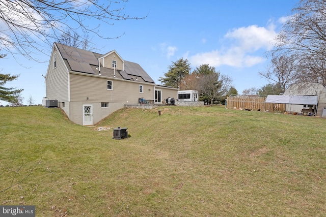 rear view of property featuring central air condition unit, a yard, and solar panels